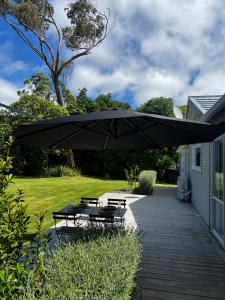 a patio with a table and benches under a large umbrella at Waihinau Cottage - One or Two Room Options! in Otaki