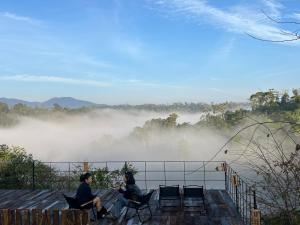 two people sitting in chairs on a deck with a view of a foggy river at Le VyN Mang Den in Kon Plong