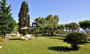 a yard with chairs and an umbrella and trees at Villa Belvedere - Panoramic Sea View apts in Vasilikos