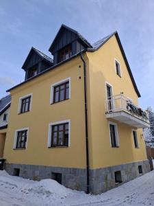 a yellow building with a balcony in the snow at U líného jezevce in Abertamy