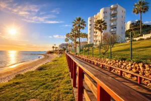 a wooden bench next to the beach with a building at Apartamento Algaida Calahonda in Sitio de Calahonda