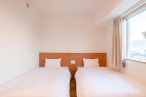 two beds in a room with a window at Smile Hotel Miyakojima in Miyako-jima