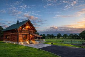 a log cabin in a field with a sunset at Log Cabin Valley - Private Villa with Pool in Gospić