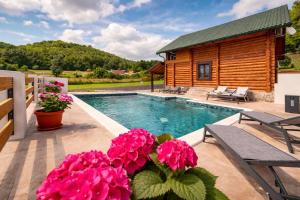 a swimming pool with a log house and pink flowers at Log Cabin Valley - Private Villa with Pool in Gospić