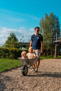a man pushing a wheelbarrow with two children in it at Landhoeve in Oosterwolde