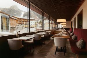 ein Restaurant mit Tischen und Stühlen und großen Fenstern in der Unterkunft The Oswald Grand Hotel in Wolkenstein in Gröden