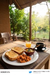 a plate of food with bread and a cup of orange juice at Almond Breeze Cottage in Udawalawe
