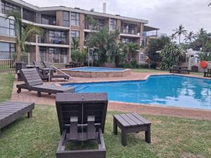 a swimming pool with benches and a building at Ocean Breeze 12 Boulder Bay in Ballito