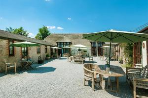 a patio with tables and chairs and umbrellas at Smugglers Cottage converted Barn with Pool & Jacuzzi NR Lyme Regis in Whitchurch Canonicorum