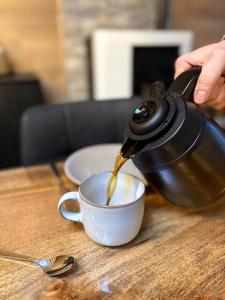 a person pouring coffee into a cup on a table at Chalet La Vallée La Boverie in Rendeux