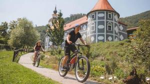two people riding bikes down a path in front of a house at KOZJANSKA KOČA in Podčetrtek