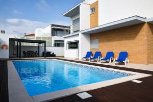 a swimming pool in front of a house with blue chairs at Nazare House4you in Nazaré