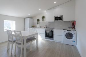 a white kitchen with a table and a washing machine at Janela do Castelo in Penela