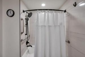 a shower with a white shower curtain and a clock at Upscale Midtown Studio and Private Balcony in Raleigh