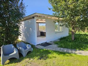 a small white building with two chairs in the grass at Domki BAMBINO in Sarbinowo +2 photos