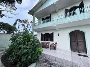 a white house with two chairs and a balcony at Casa espaçosa 100m da praia in Ubatuba
