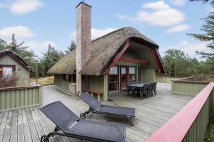 a house with a thatched roof with chairs on a deck at 602-Hvide-Sande-Nygardsvej-32 in Bjerregård