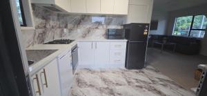 a kitchen with white cabinets and a black refrigerator at Paradise on Snells Beach in Snells Beach