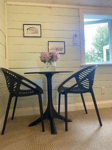 a table with two chairs and a vase with flowers on it at Pinegrove Cottage - Greytown Getaway in Woodside