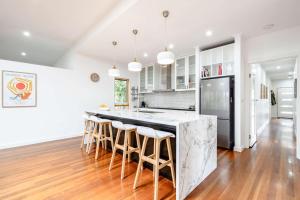 a kitchen with a large island with bar stools at The Greenhouse - Spa & Fire - Pet Friendly in Barwon Heads +23 photos