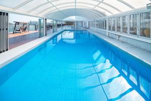 a large swimming pool with blue water in a building at Yeosu K-Park Spa Pension in Yeosu