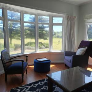 a living room with a couch and chairs and windows at Little Blue Bach in Whanganui