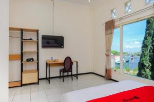 a bedroom with a bed and a desk and a television at RedDoorz at Jestro Guest House Batu in Tlekung