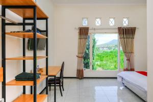 a bedroom with a bed and a desk and a window at RedDoorz at Jestro Guest House Batu in Tlekung