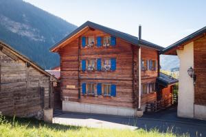 a wooden house with blue windows in a mountain at Chalet Regenbogen Familienapartment mit Indoor-Rutschbahn & Spieloase an der Fussgängerzone in Leukerbad