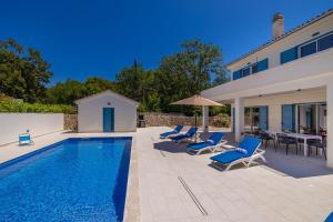 a swimming pool with blue chairs and a house at Holiday house DAN with private pool in Kras