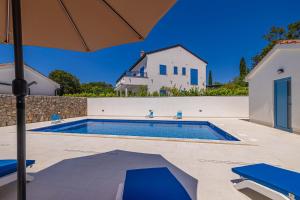 a swimming pool with an umbrella next to a house at Holiday house DAN with private pool in Kras