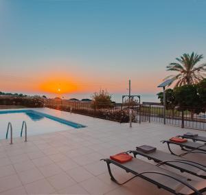 a swimming pool with two lounge chairs and a sunset at Villa Hera in Ayios Theodhoros