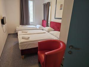 a room with two beds and a red chair at Hotel Astral Vienna in Vienna