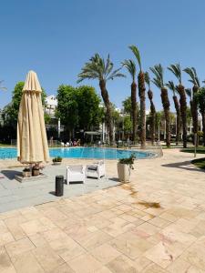 a pool with two chairs and a umbrella and palm trees at Royal Park A&7 Deluxe, swim pool - by G&P suites in Eilat