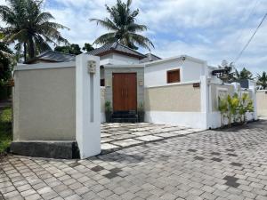 a white house with a door and a brick driveway at Peony Villa Lovina in Lovina
