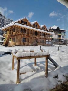 a wooden house in the snow with a bench in front at Kabir's Chalet Shangarh in Shangarh +35 photos