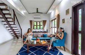 two women sitting in a living room on their phones at EKOSTAY Luxe - Oceanic Villa in Alibaug