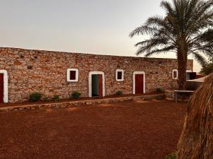 a brick building with red doors and a palm tree at Auberge Nasser in Chinguetti