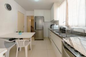 a white kitchen with a table and a refrigerator at Espaçoso e Confortável Próximo da UEM - EL08 in Maringá