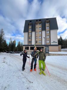 three people standing in the snow in front of a building at Apartement LUNA Hotel Zlatni javor in Jahorina