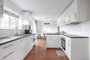 a white kitchen with white cabinets and a wooden floor at 3 Bedroom Spacious Bella Range Homes in Hornchurch