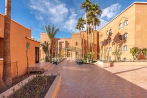 a building with palm trees and a brick sidewalk at Kenzi Azghor in Ouarzazate
