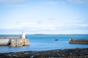 a boat in a body of water with a lighthouse at Northern Hideaways, Eider Cottage, Seahouses in Seahouses