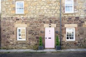 a stone building with a white door and two windows at Northern Hideaways, Eider Cottage, Seahouses in Seahouses
