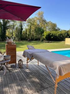 a bed and an umbrella on a deck next to a pool at Le Clos des Eaux in Tailly