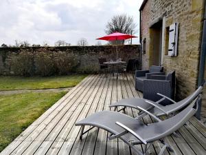 a wooden deck with chairs and a table with an umbrella at Gîte Le Val de Marigny 2 personnes in Longues-sur-Mer