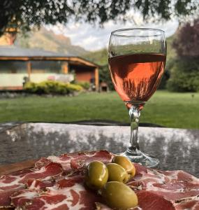a glass of wine next to a plate of meat and grapes at Hostería Meliquina in Lago Meliquina