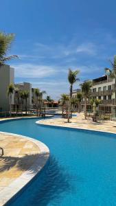 a large blue swimming pool with palm trees and buildings at Brisa Rooftop Vistamar -Apartamento à beira mar com jacuzzi in Luis Correia