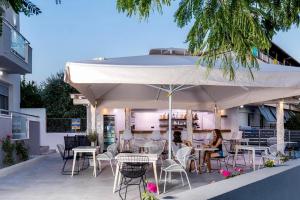 two people sitting at tables under an umbrella on a patio at Lena Apartments Potos Thassos in Potos