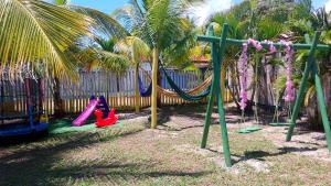 a playground with swings and palm trees and a fence at Chalé a beira mar ilhéus in Ilhéus